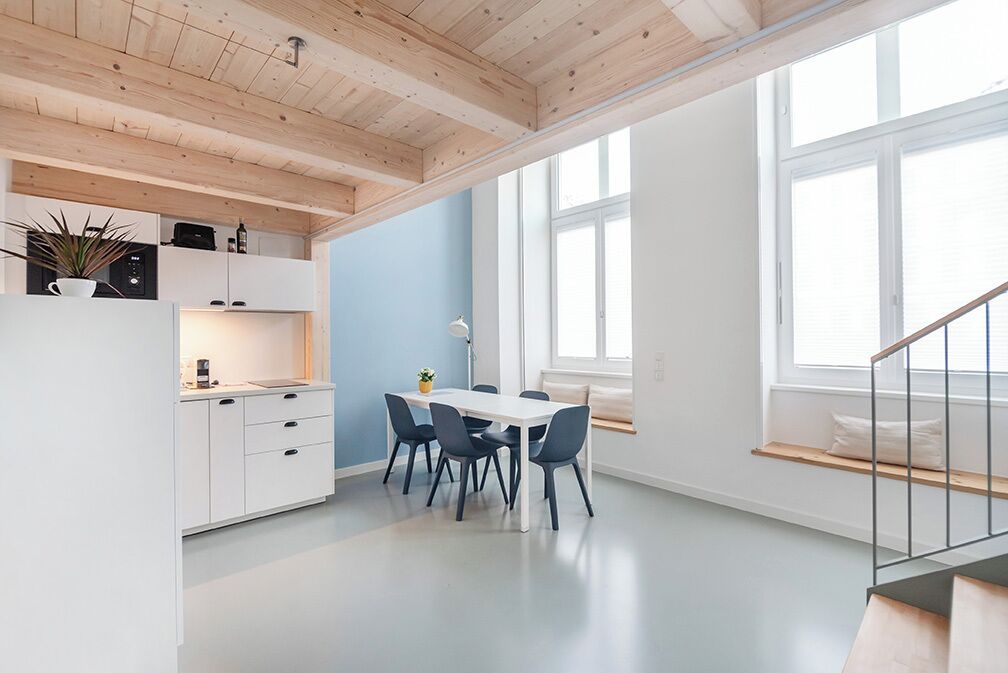 A modern kitchen with white cabinets, a dining table with chairs, and a built-in oven.