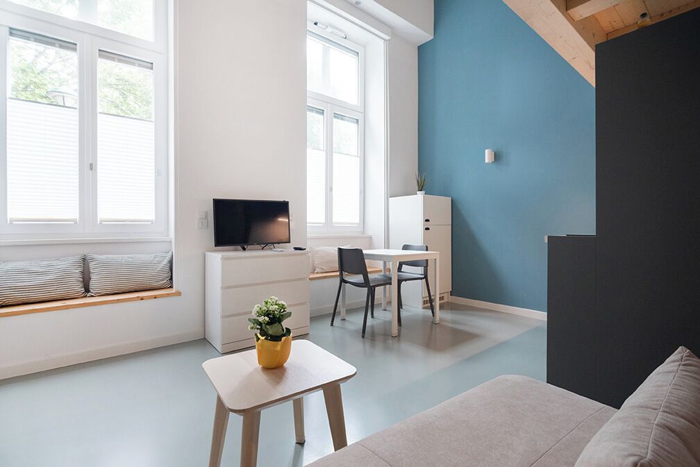 Una sala de estar moderna con un sofá, una mesita con una planta, un televisor y un escritorio con sillas.