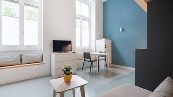 Una sala de estar moderna con un sofá, una mesita con una planta, un televisor y un escritorio con sillas.