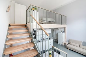 Un intérieur moderne avec un escalier en bois, une chambre en mezzanine, un coin cuisine et un espace de vie doté d’un canapé.