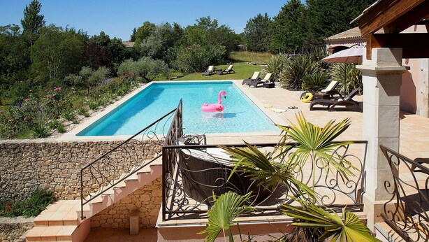 Piscina com um flutuador em formato de flamingo rosa, rodeada por cadeiras de descanso e uma escadaria de pedra que leva a uma área coberta.