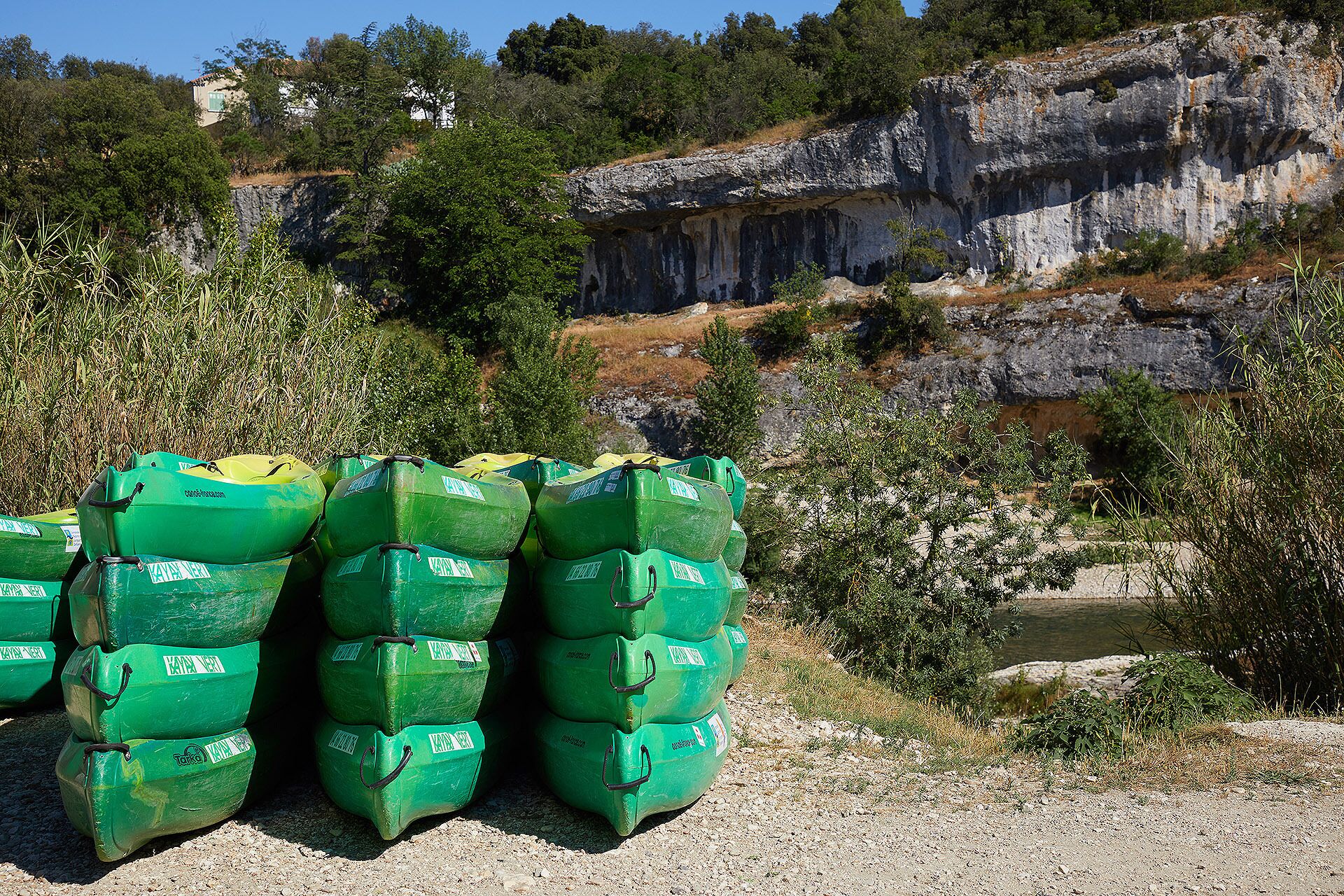 Stacks of green containers in a natural setting with rocky cliffs and vegetation.