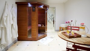 Um quarto com sauna, um banco de madeira, uma mesa com bandeja e um vaso com flores.