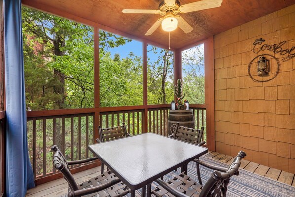 A covered outdoor patio with a table and chairs, a ceiling fan, and a wooden wall with a "Cowboy" sign.