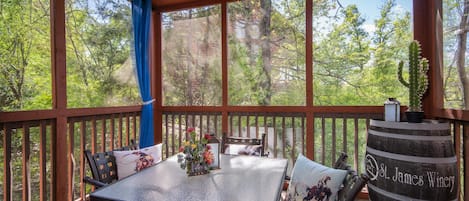 A covered outdoor deck with a table and chairs, a wooden barrel labeled "St. James Winery," and a view of trees through large windows.