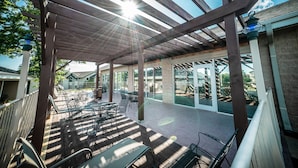 Een terras buiten met houten pergola, tafels en stoelen.