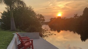 A sunset view over a calm body of water with a concrete deck and red chairs.