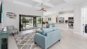 A spacious living area with a light blue sofa, a dining table, and a kitchen in the background.