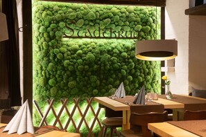 A restaurant interior with a green moss wall, wooden tables, and chairs. - Hotel Stadtkrug (Weiden in der Oberpfalz)