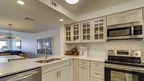 Una cocina moderna con armarios blancos, electrodomésticos de acero inoxidable y un comedor con mesa y sillas.