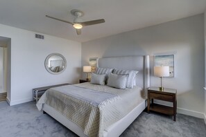 A bedroom with a bed, bedside tables, a ceiling fan, a mirror, and two wall-mounted lamps.
