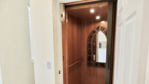 A narrow hallway with a wooden elevator door and a small mirror on the wall. - Luxury Gulf Beach Living - Coronas Gris (Siesta Key)
