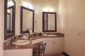 A bathroom with two sinks, a chair, and a large mirror.
