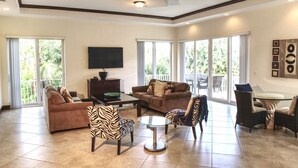 A spacious living room with a brown sofa, zebra-patterned chairs, a glass coffee table, and a flat-screen TV mounted on the wall. - Luxury Gulf Beach Living - Coronas Gris (Siesta Key)
