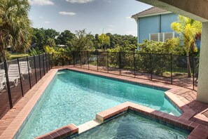 A rectangular swimming pool with a tiled edge, surrounded by a black fence and a brick border.