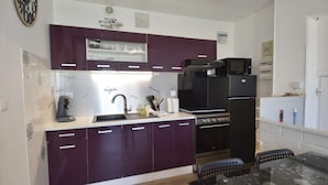 A modern kitchen with purple cabinets, a black refrigerator, and a microwave.