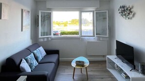 A modern living room with a sofa, a coffee table, a TV stand, and a window with a view of the outside.