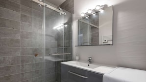 A modern bathroom with a glass-enclosed shower, a white sink, and a built-in mirror with lights.