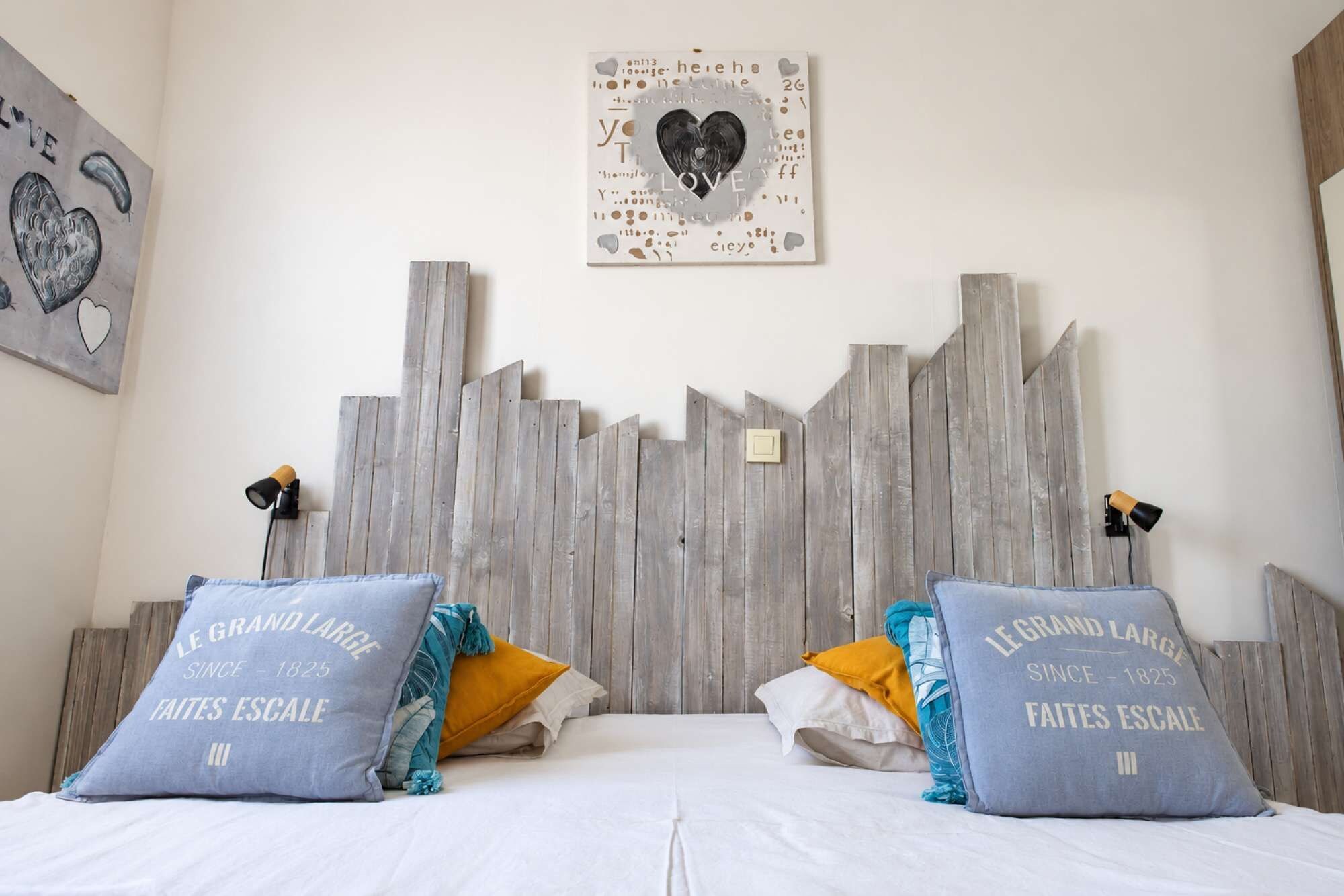 A bedroom with a bed, pillows, a wall art piece, and a wooden headboard.