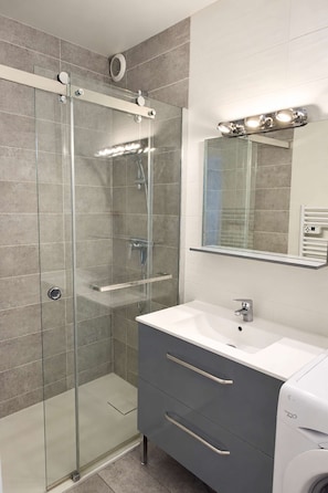 A modern bathroom with a glass shower enclosure, a white sink, and a vanity with a mirror.