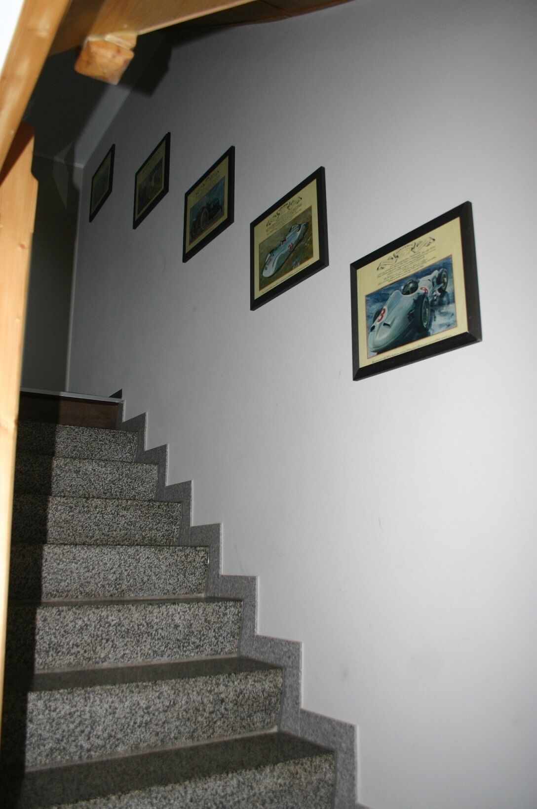 A staircase with granite steps leading to a landing where four framed pictures are hung on the wall.