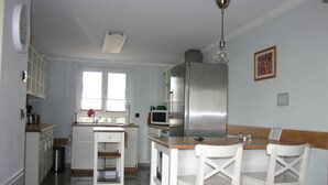 A kitchen with white cabinets, a stainless steel refrigerator, a microwave, and a sink. There is a window with blinds, a ceiling light, and a picture on the wall. - Quartier78 - Welcome to friends in Mittweida  (Mittweida)
