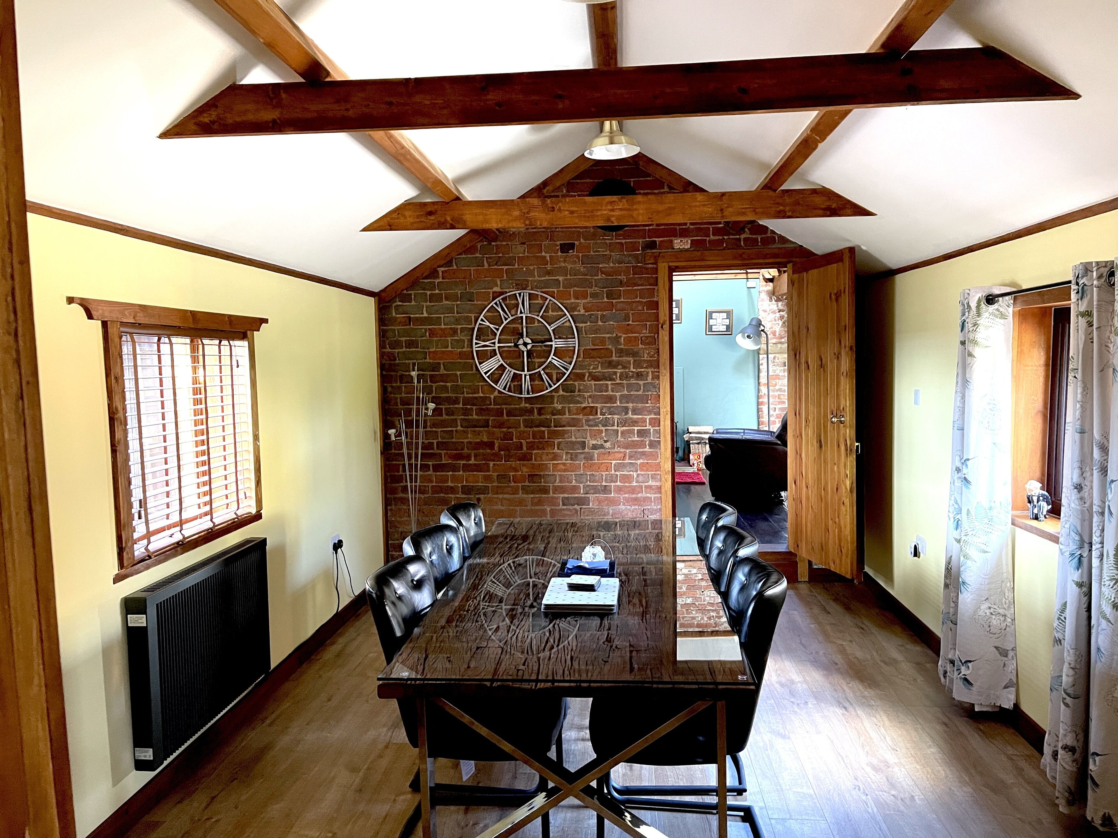 A dining room with a wooden table, leather chairs, a brick wall, and a large clock.