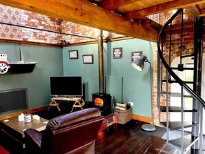 A cozy living room with a fireplace, a television, and a spiral staircase. - 2-bed 18th Century Barn - Sleeps 6 - Pet Friendly (Boston)