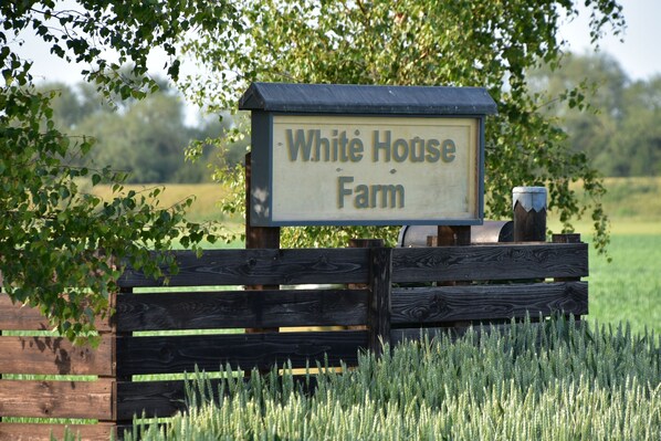 Une enseigne en bois portant l’inscription « White House Farm », située dans un cadre rural.