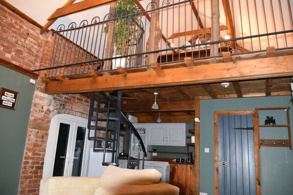 A rustic interior with exposed wooden beams, a brick wall, and a staircase leading to a loft area. - 2-bed 18th Century Barn - Sleeps 6 - Pet Friendly (Boston)