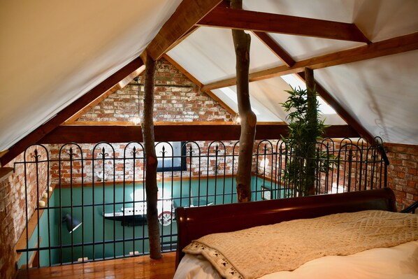 A bedroom with a view of a swimming pool, a wooden ceiling, and a brick wall. - 2-bed 18th Century Barn - Sleeps 6 - Pet Friendly (Boston)