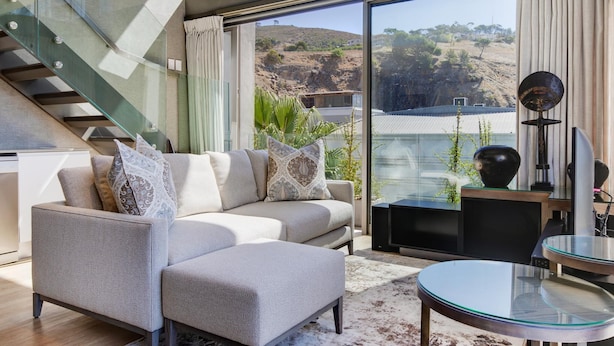 A modern living room with a sofa, glass coffee table, and a staircase. - Always-Power Stunning Apartment with 180 Degree City View near V&A Waterfront (Cape Town)