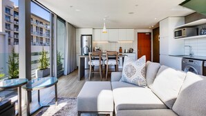 A modern apartment with a kitchen, dining area, and living room. It features large windows, a sofa, and a glass table. - Always-Power Stunning Apartment with 180 Degree City View near V&A Waterfront (Cape Town)