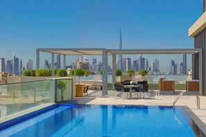 Une piscine sur le toit offrant une vue panoramique sur la ville, des espaces de détente en plein air et une balustrade en verre.