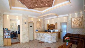 A lobby with a reception desk, a brown leather sofa, a coffee table, and a bookshelf. - Elpis Studios And Apartments (Mylopotamos)
