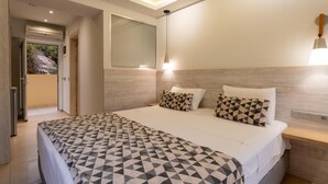 A modern bedroom with a large bed, geometric-patterned bedding, a bedside table, a nightstand, a wall-mounted mirror, and recessed ceiling lighting. - Elpis Studios And Apartments (Mylopotamos)