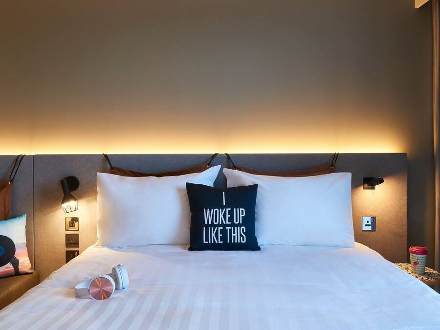 A neatly made bed with a pillow that reads "I woke up like this."
