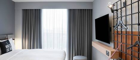A modern hotel room with a large bed, a TV mounted on the wall, and a window with curtains.