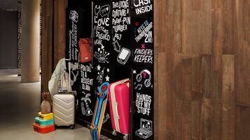 Entrada de hotel con interior de madera y pared negra con texto e ilustraciones blancas. Hay maletas y una mochila cerca de la entrada.