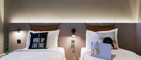 Camera d'albergo con due letti, ognuno con un cuscino, un comodino con un portatile, una bottiglia e un quaderno.