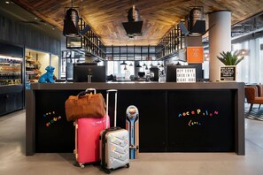 A reception desk with a black counter, a blue mascot figure, and a skateboard. There are suitcases and a handbag on the counter.