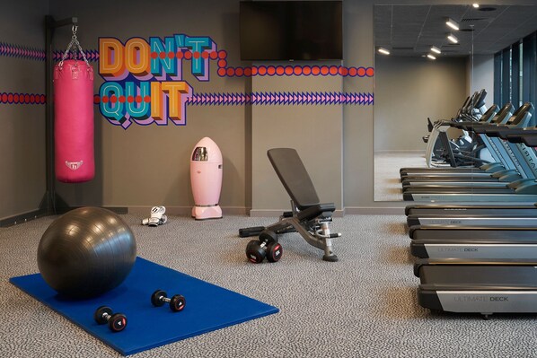 Un gimnasio con equipamiento de ejercicio, un saco de boxeo y un letrero de motivación en la pared.