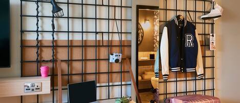 A room with a desk, laptop, pink suitcase, and a hanging coat rack with a jacket.