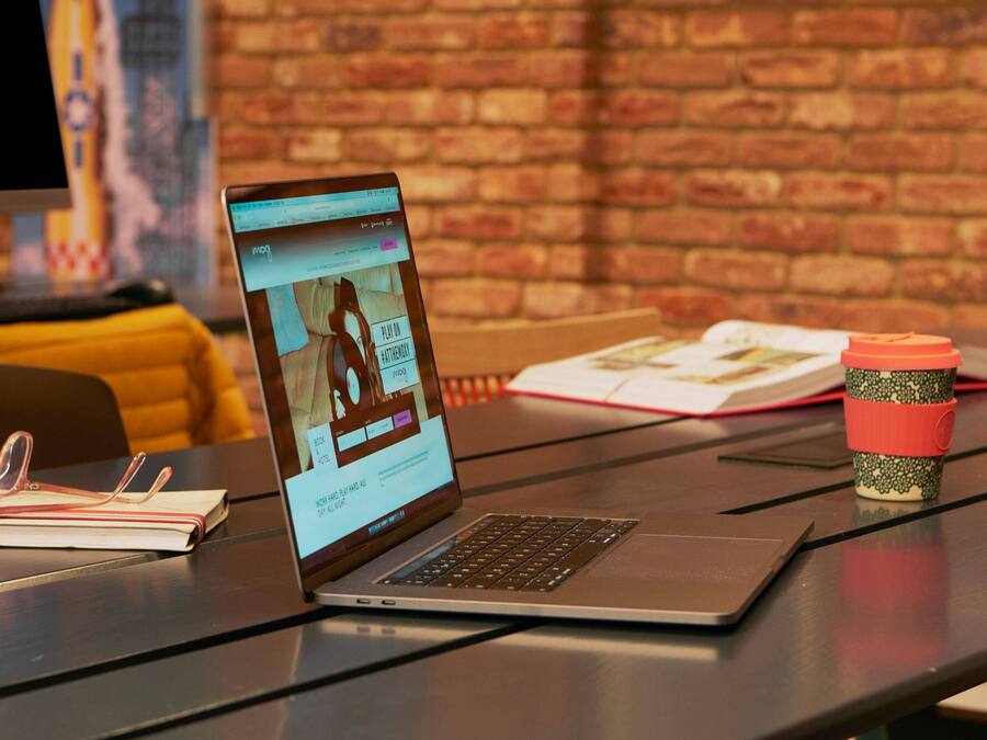 Una computadora portátil sobre una mesa, junto con un cuaderno, lentes y una taza de café.