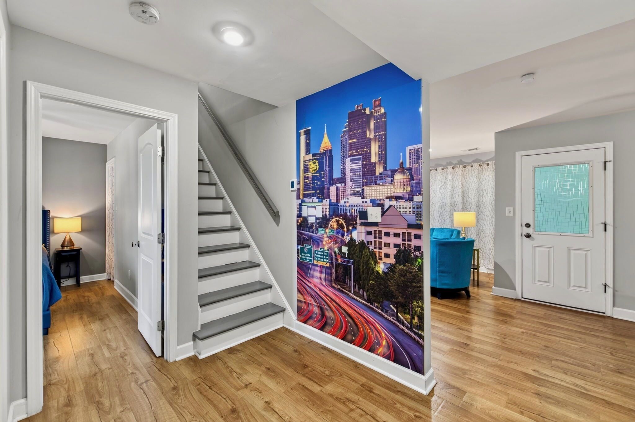 A modern interior with a staircase, a cityscape mural, and a blue chair.