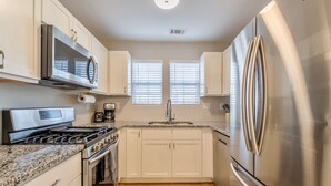 A modern kitchen with stainless steel appliances, white cabinetry, and a granite countertop.