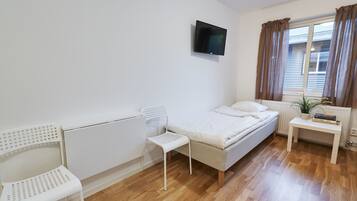 A small, clean room with a bed, a chair, a TV, and a window with curtains.