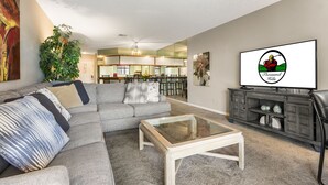 Una sala moderna con un sofá modular, una mesa de centro de cristal y un televisor mostrando un logotipo.