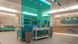 A modern hotel lobby with a reception desk, seating area, and a glass partition. - Estia Hotel (Pylos-Nestoras)
