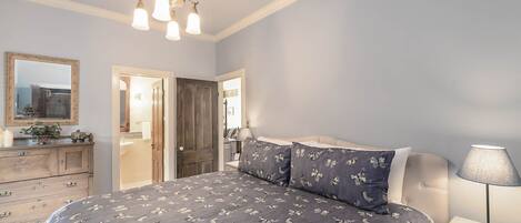 A bedroom with a bed, bedside table, lamp, dresser, and a mirror.